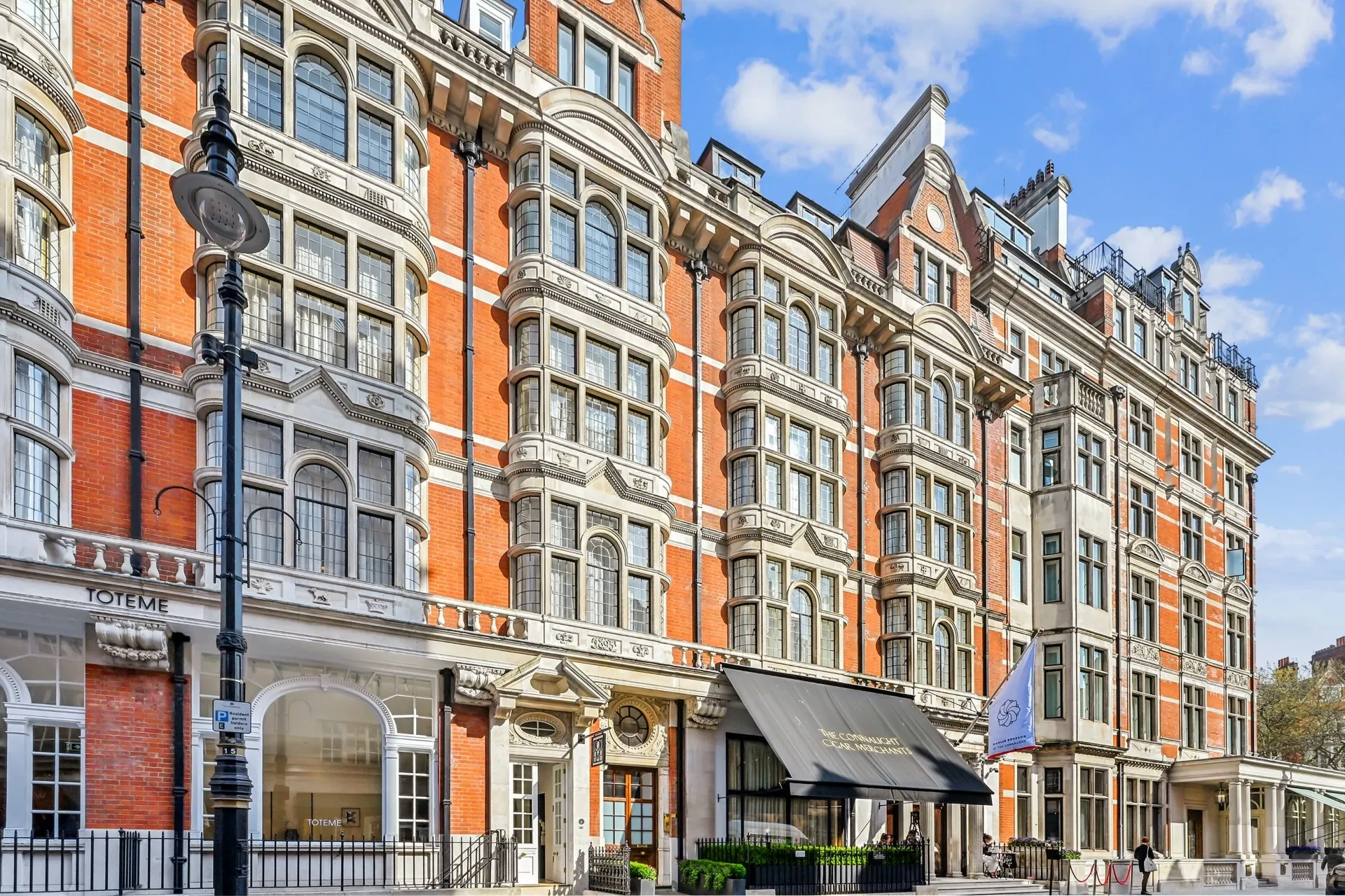 Exterior of a grand red-brick building with bay windows, black awning, and hotel entrance.