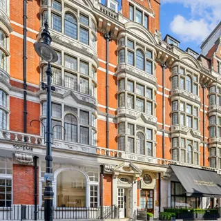Exterior of a grand red-brick building with bay windows, black awning, and hotel entrance.