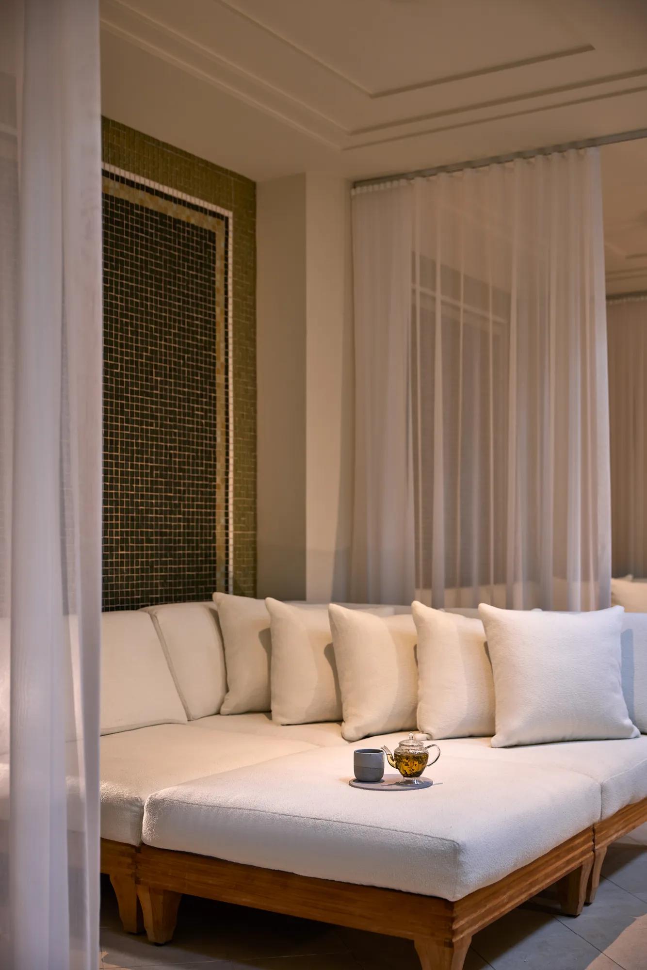 Private spa lounge with soft white daybed, sheer curtains, and herbal tea service