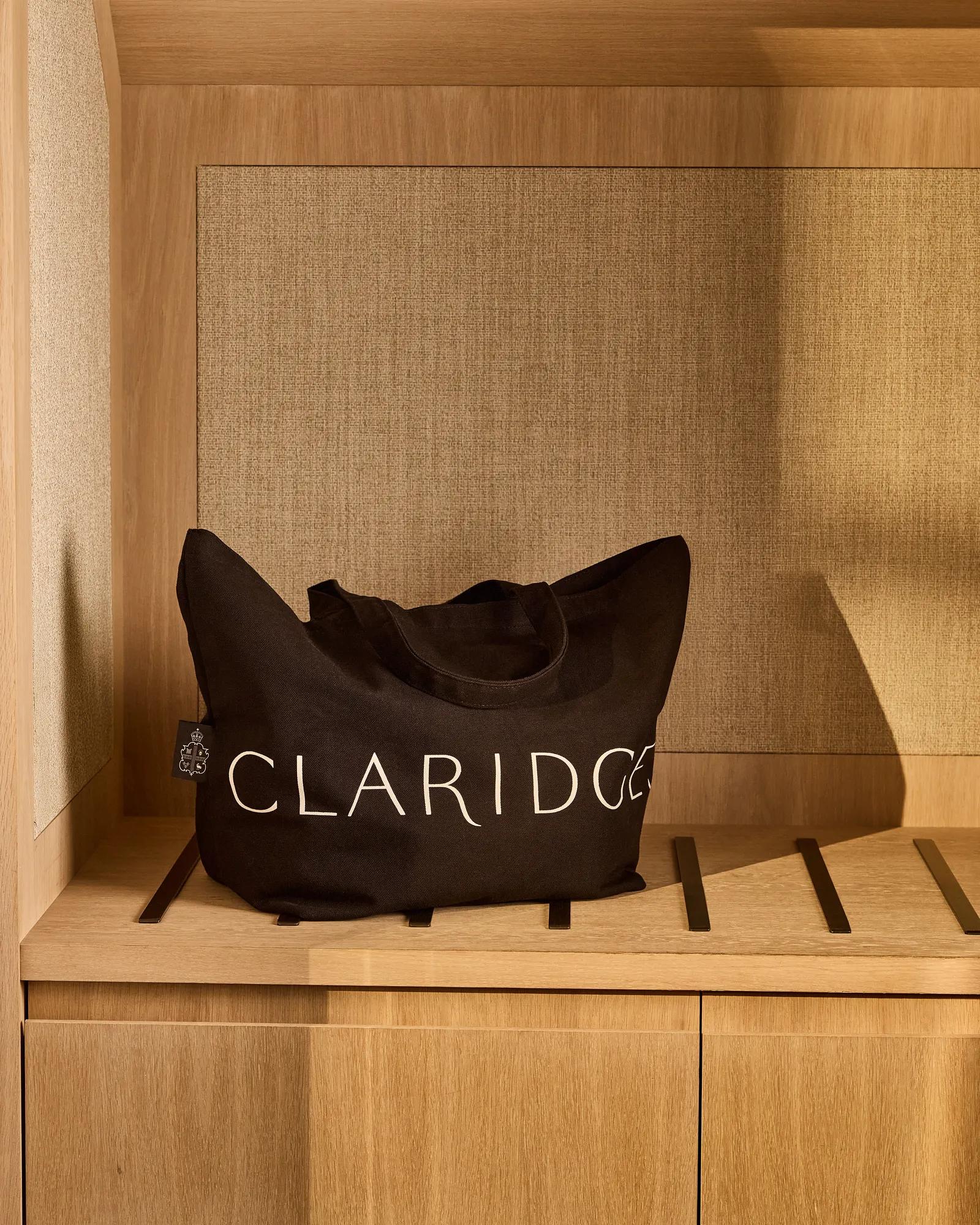 Black Claridge’s branded tote bag resting on a wooden shelf within a softly lit wardrobe alcove.