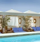 Cabanas and blue loungers lining The Maybourne Beverly Hills rooftop pool beneath white canopies.