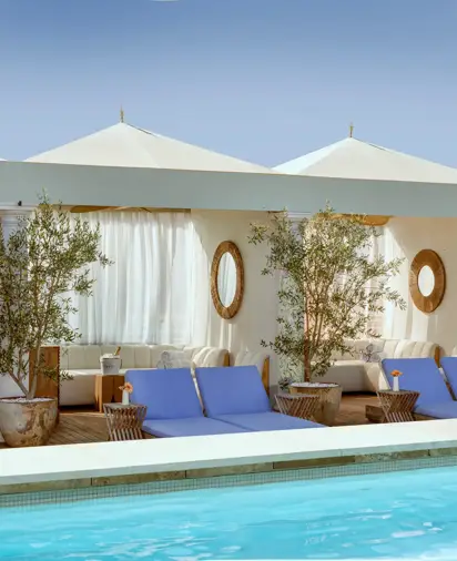 Cabanas and blue loungers lining The Maybourne Beverly Hills rooftop pool beneath white canopies.