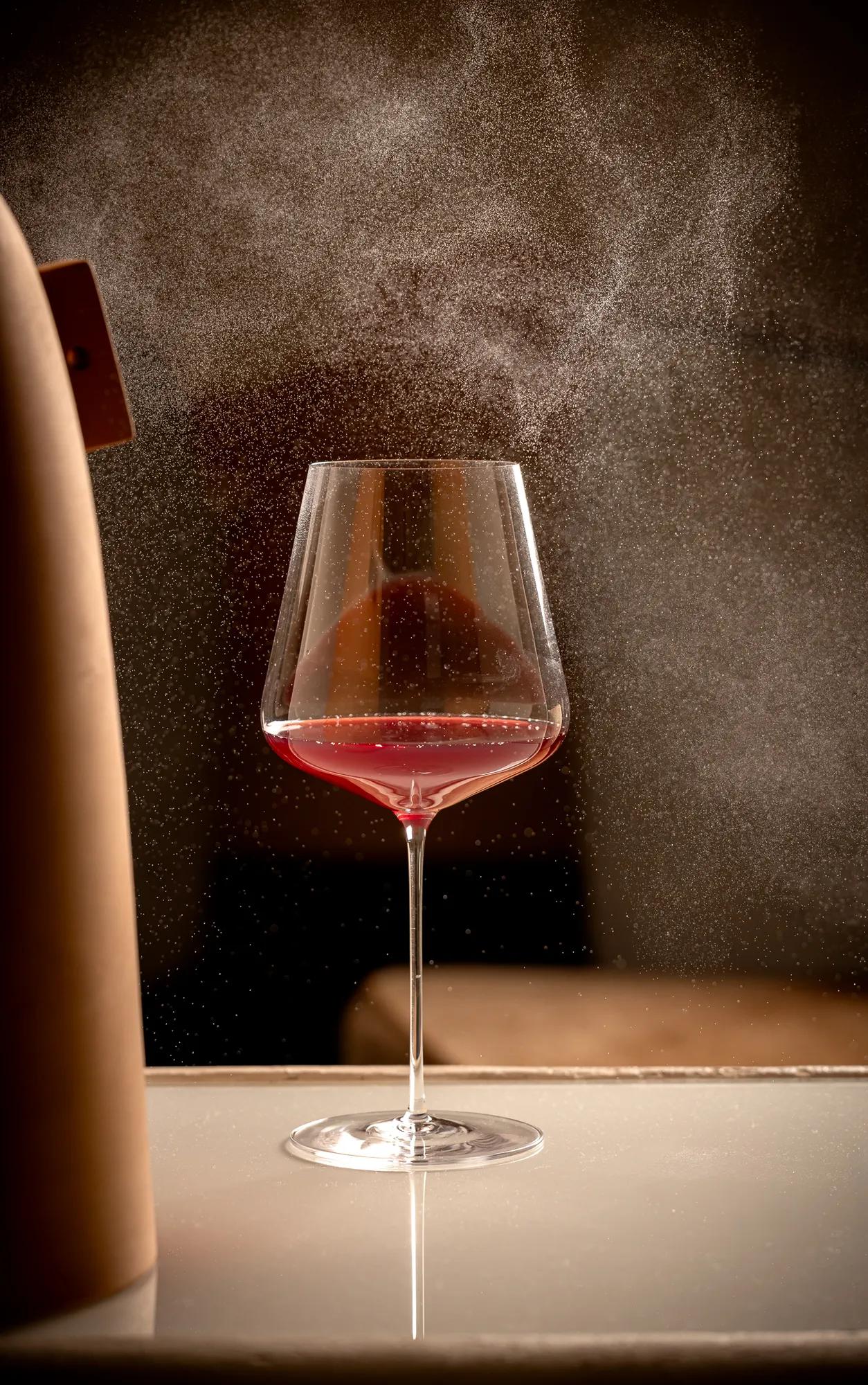 Glass of red wine on a reflective surface as a fine mist sprays around it.