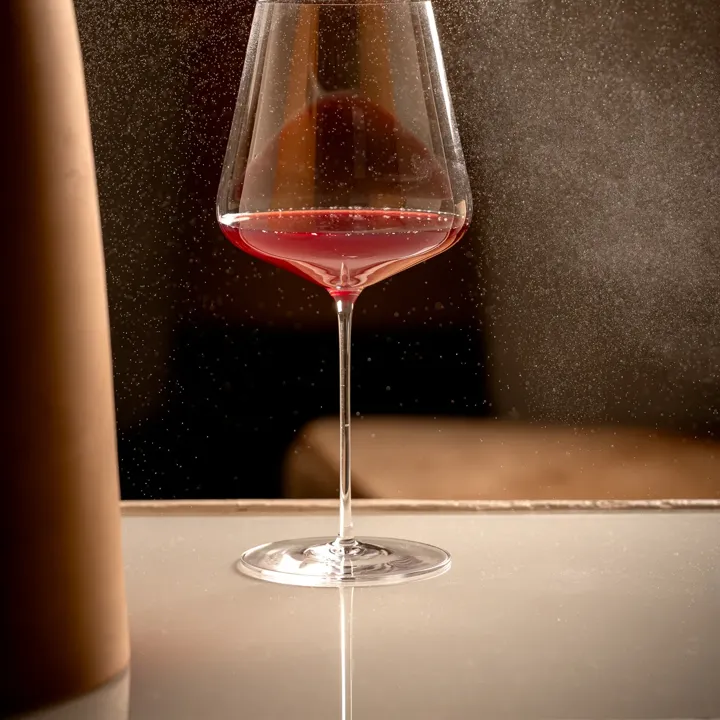 Glass of red wine on a reflective surface as a fine mist sprays around it.