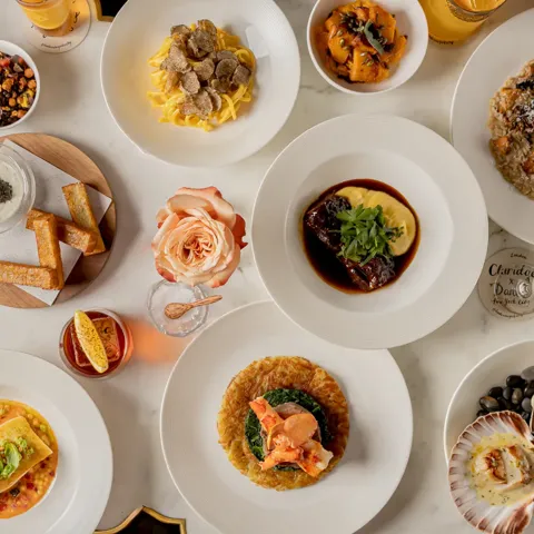Overhead view of a table set with plated dishes, pasta, seafood, salads, bread, and drinks arranged for shared dining.