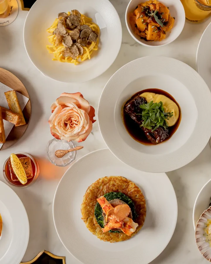 Overhead view of a table set with plated dishes, pasta, seafood, salads, bread, and drinks arranged for shared dining.