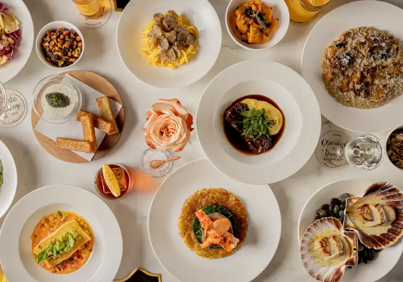 Overhead view of a table set with plated dishes, pasta, seafood, salads, bread, and drinks arranged for shared dining.