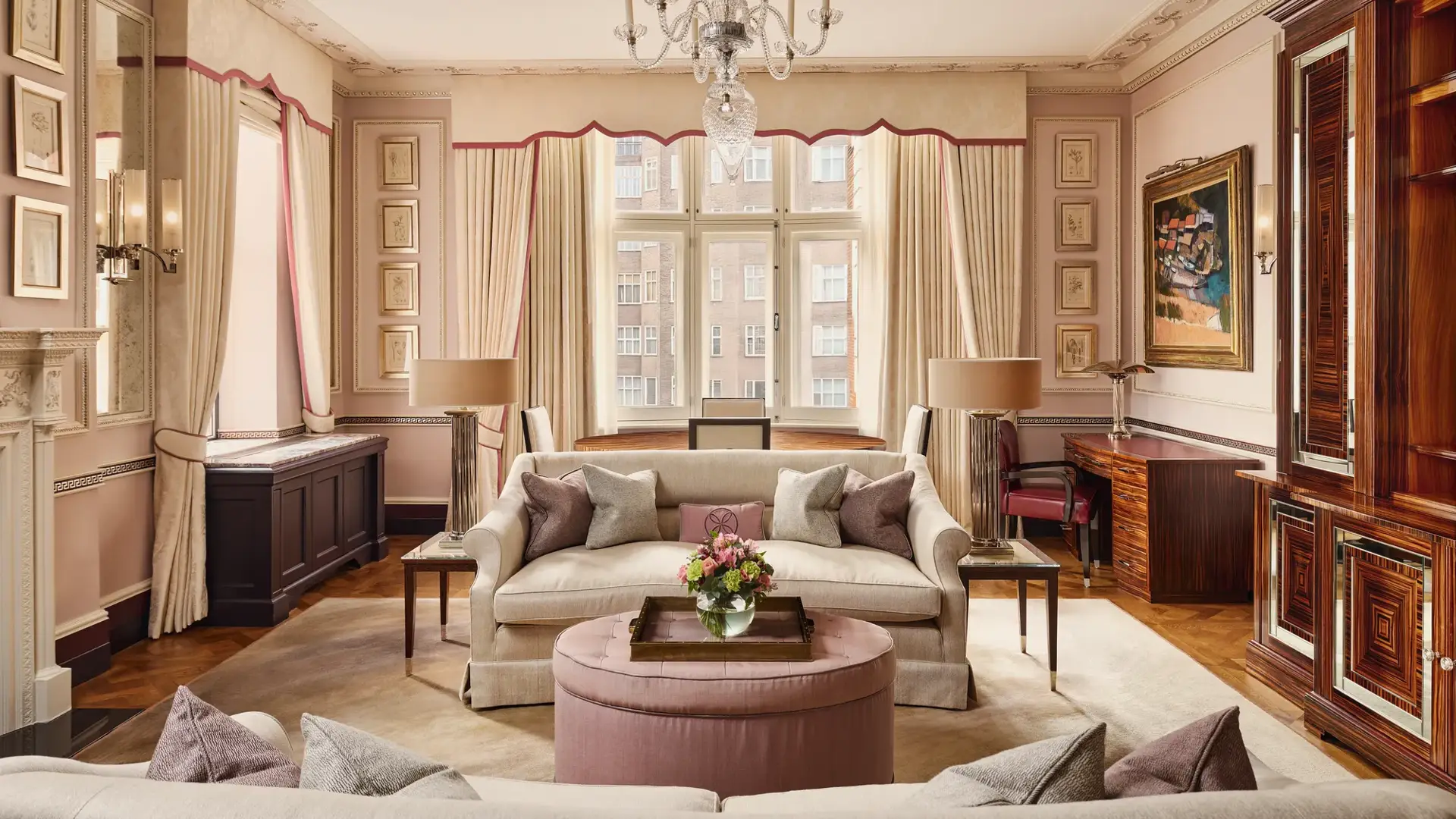 Grand living room with cream sofas, chandelier, large window, and pink accents.