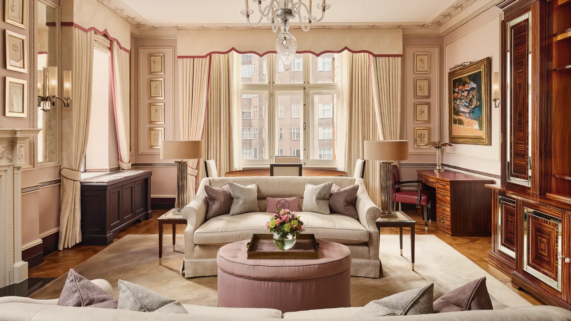 Grand living room with cream sofas, chandelier, large window, and pink accents.
