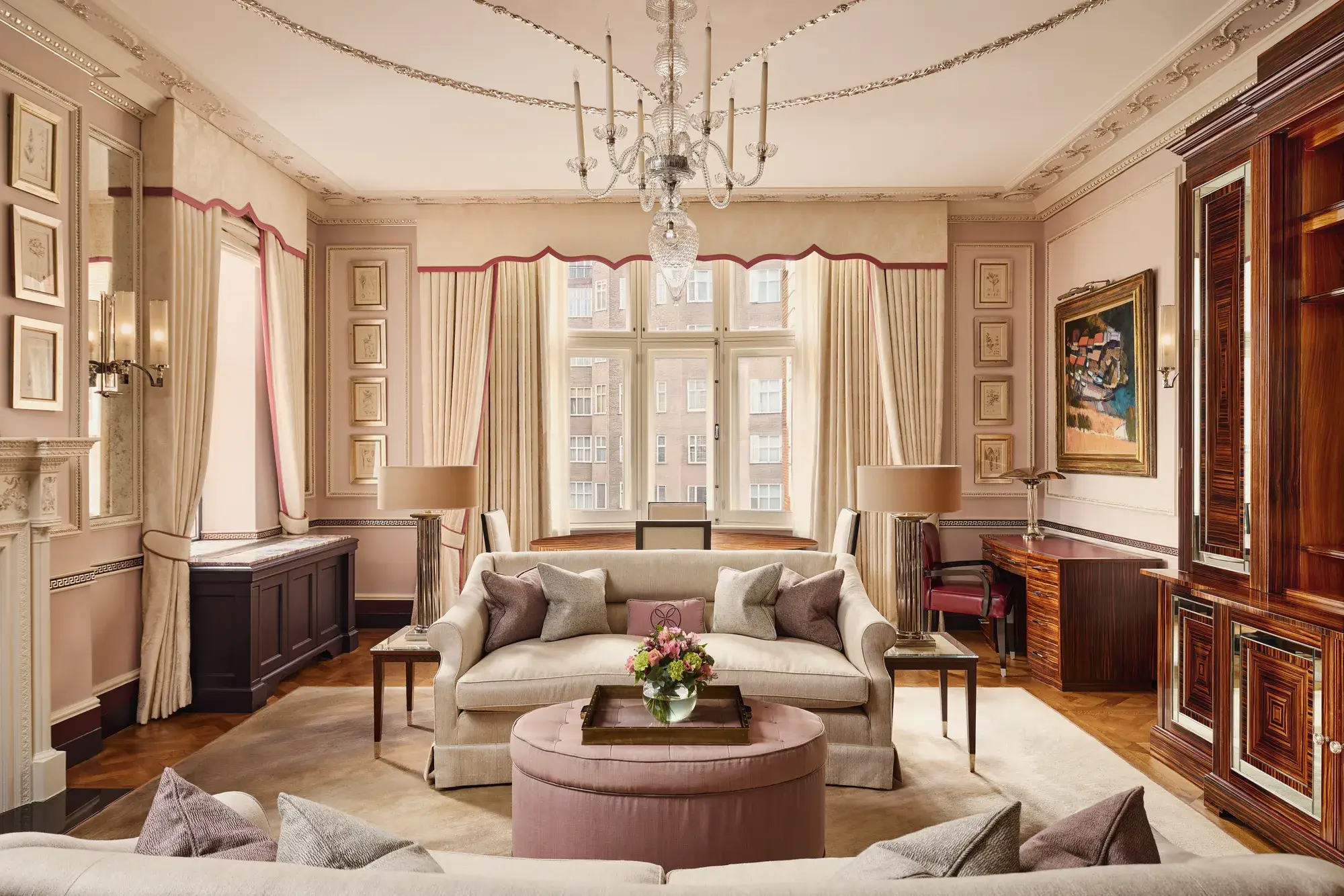 Grand living room with cream sofas, chandelier, large window, and pink accents.