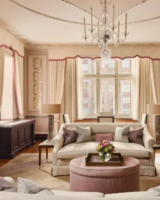 Grand living room with cream sofas, chandelier, large window, and pink accents.