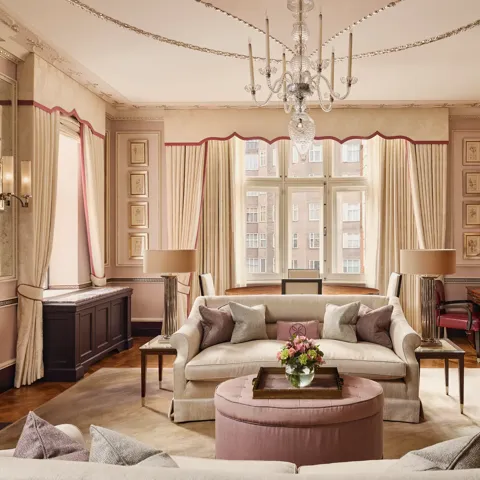 Grand living room with cream sofas, chandelier, large window, and pink accents.