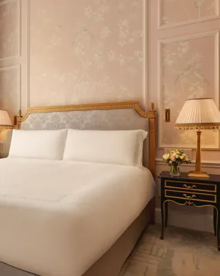 Elegant bedroom with king bed, pink floral walls, bedside lamps, and tall window.