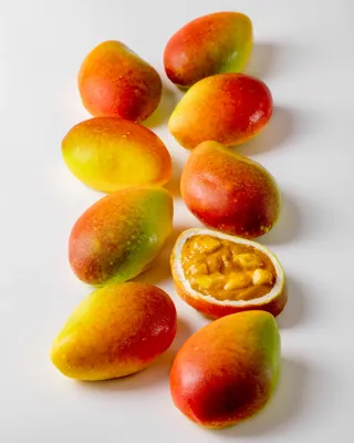 Passion fruit–shaped cakes on a white surface, one cut open to reveal a golden, mousse-like filling.