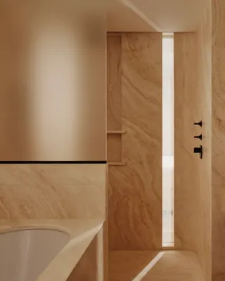 Luxury bathroom with marble walls, walk-in shower, freestanding bath edge, double vanity and warm wood cabinetry.