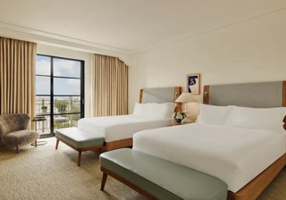 Spacious hotel room with two queen beds, seating area, and balcony doors.