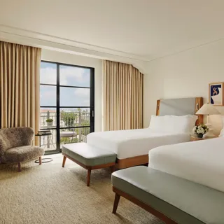 Spacious hotel room with two queen beds, seating area, and balcony doors.