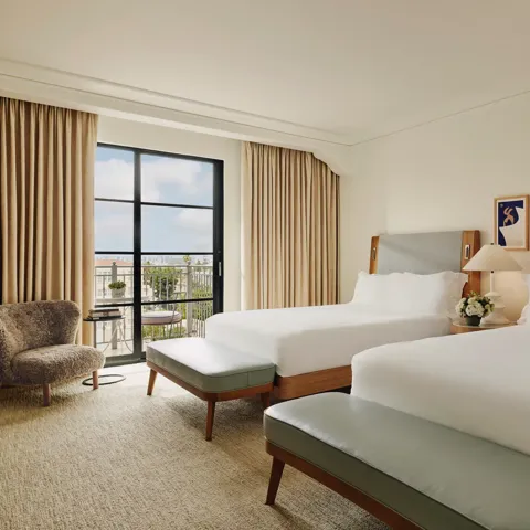 Spacious hotel room with two queen beds, seating area, and balcony doors.