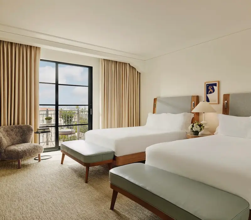 Spacious hotel room with two queen beds, seating area, and balcony doors.