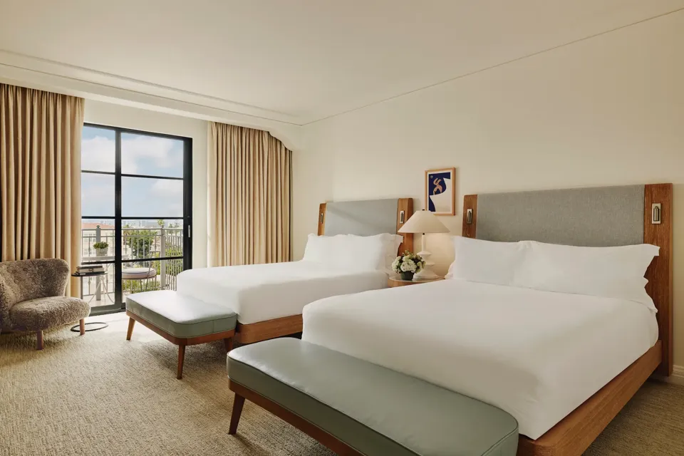 Spacious hotel room with two queen beds, seating area, and balcony doors.