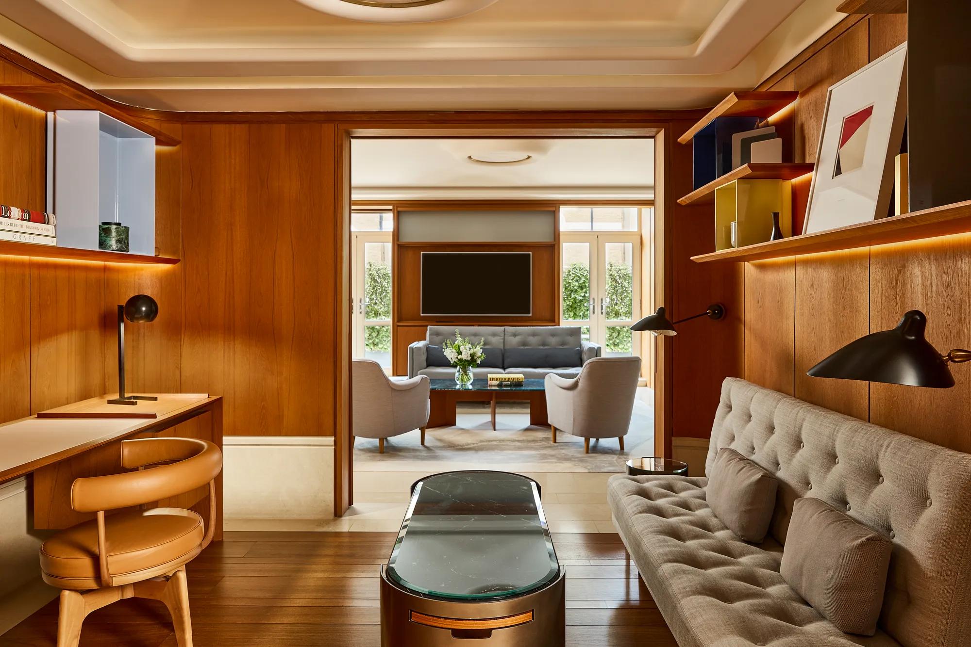 Wood-panelled study with desk and sofa opening into a bright lounge with armchairs and garden views.