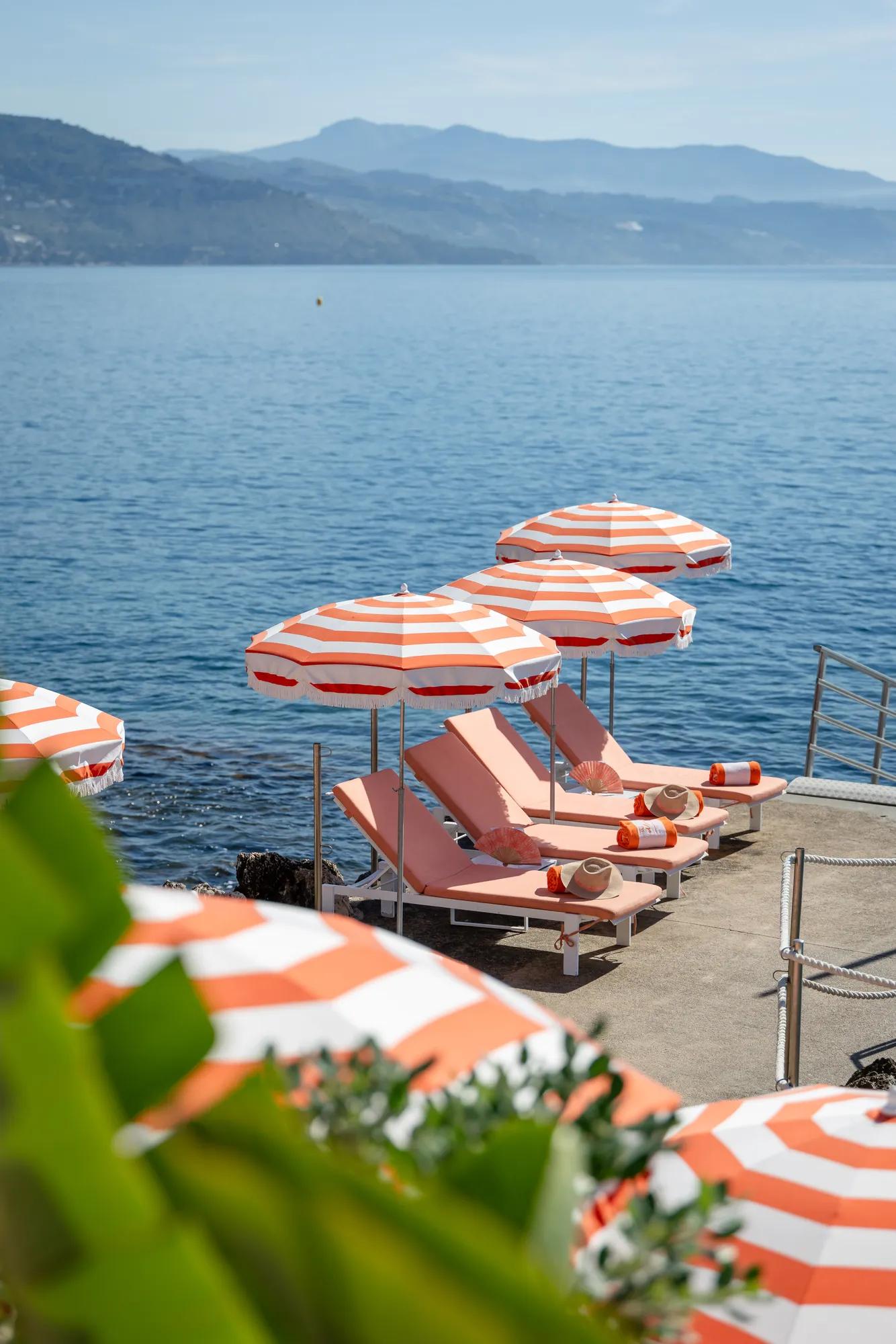 Parasols rayés orange et blanc avec transats sur une terrasse au bord de la mer.