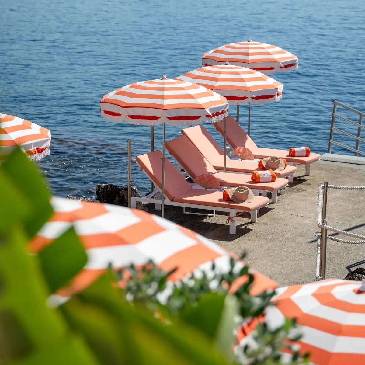 Parasols rayés orange et blanc avec transats sur une terrasse au bord de la mer.