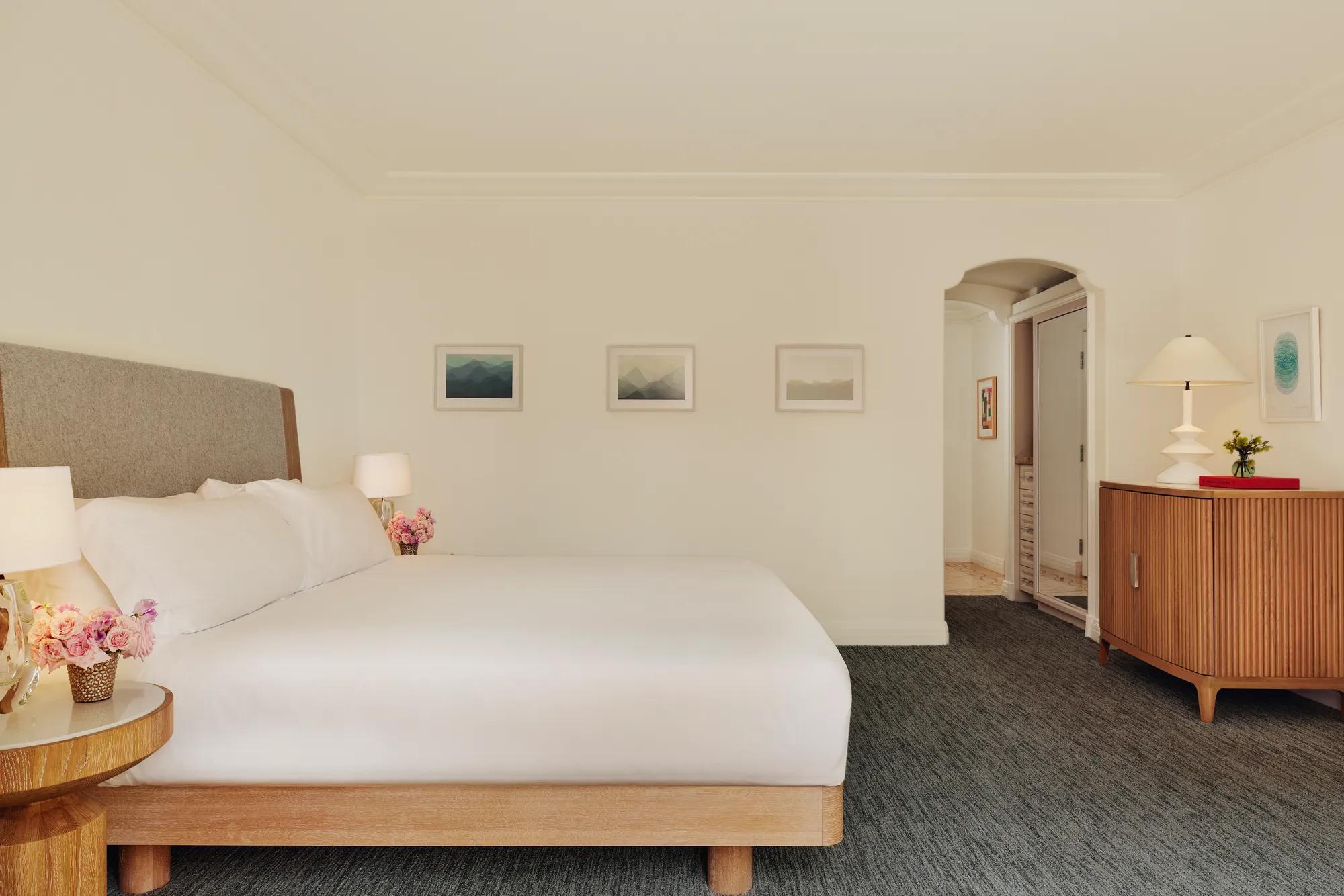 Accessible king bedroom with upholstered headboard, three framed prints, dresser with lamp, and an arched doorway to the bathroom.