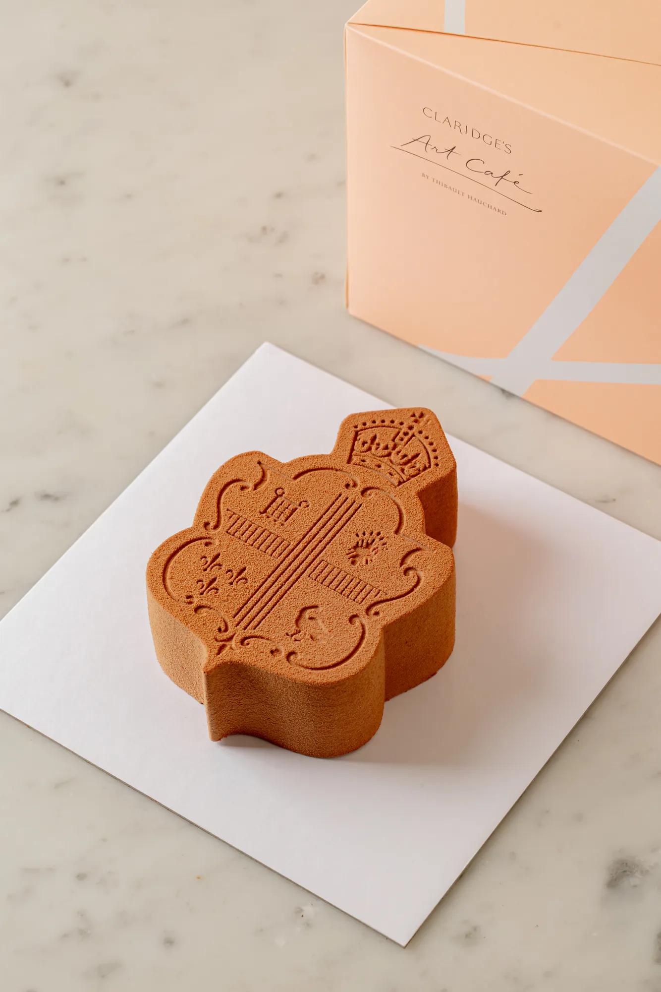 A Claridge’s Art Cake displayed on a marble table beside a branded presentation box.