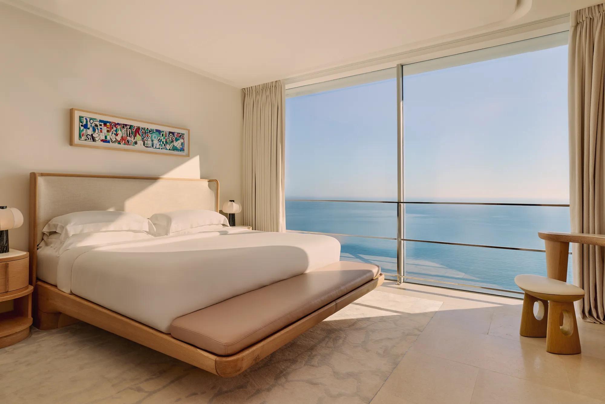 Chambre élégante avec grand lit, mobilier en bois clair et baies vitrées offrant une vue panoramique sur la mer.