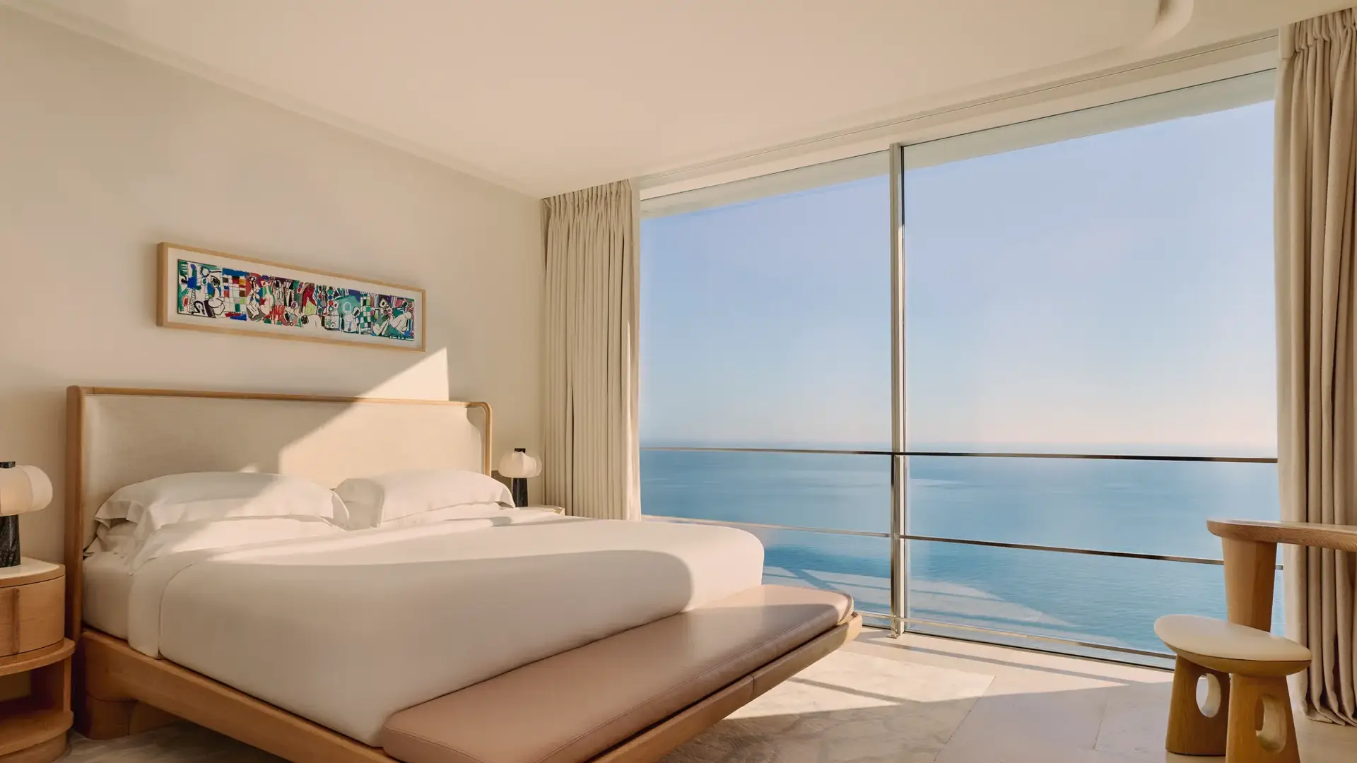 Chambre élégante avec grand lit, mobilier en bois clair et baies vitrées offrant une vue panoramique sur la mer.
