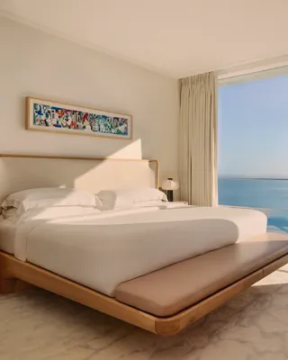 Chambre élégante avec grand lit, mobilier en bois clair et baies vitrées offrant une vue panoramique sur la mer.
