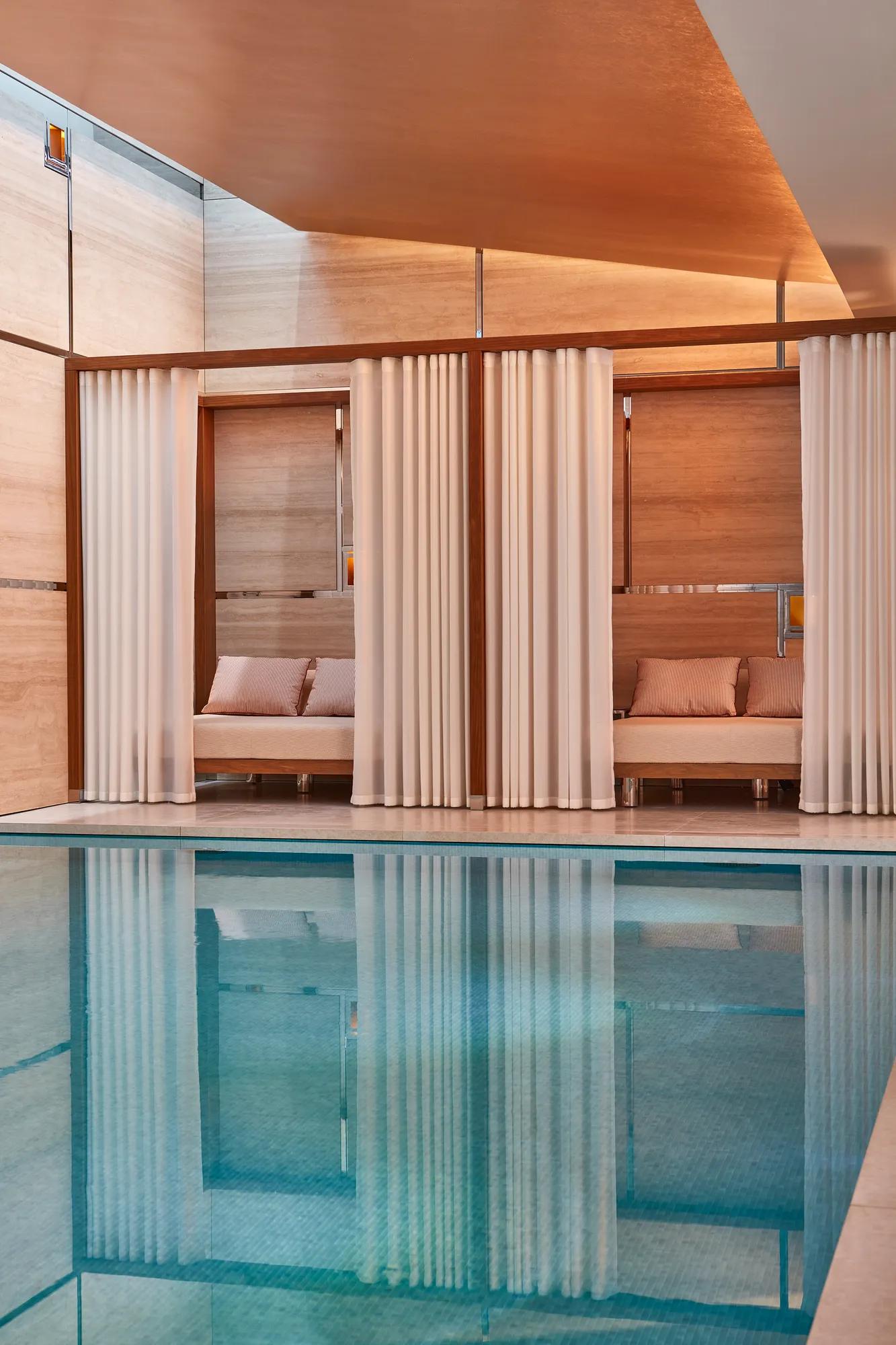 Tranquil spa pool with curtained daybeds, warm lighting, and natural-toned wall panelling.