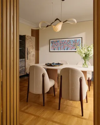 Elegant dining space with a white marble table, upholstered chairs, and a sculptural chandelier above.