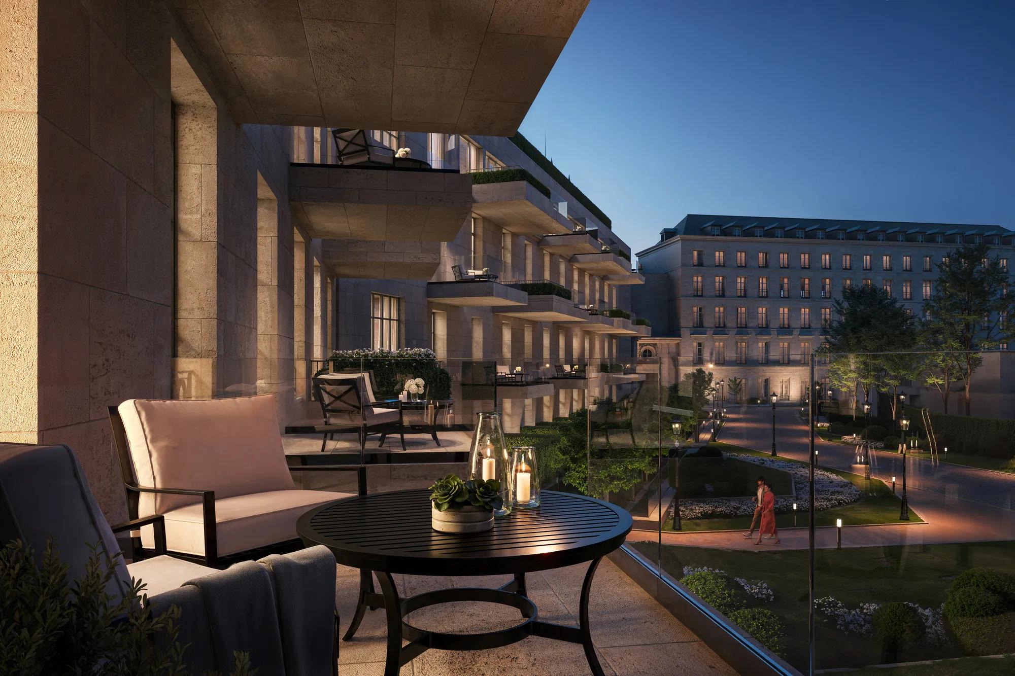 Private balcony with armchairs and candlelit table overlooking landscaped courtyard and elegant hotel building at dusk