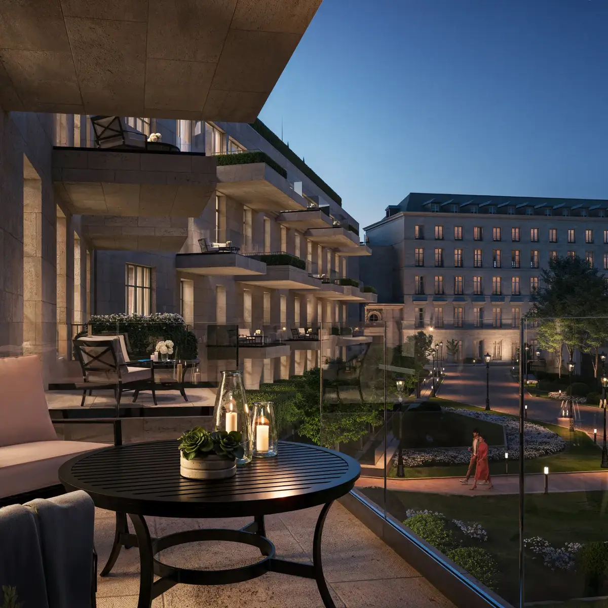Private balcony with armchairs and candlelit table overlooking landscaped courtyard and elegant hotel building at dusk