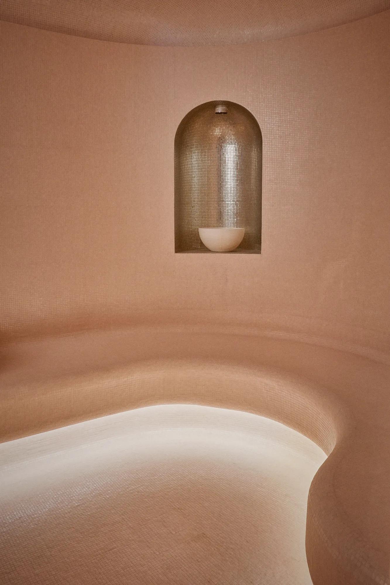 Curved steam room seating with soft lighting, textured walls, and recessed niche lamp creating a warm, calming spa atmosphere.
