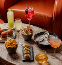 Marble table with oysters, sliders, fries, small tacos, and assorted cocktails in colourful glassware.