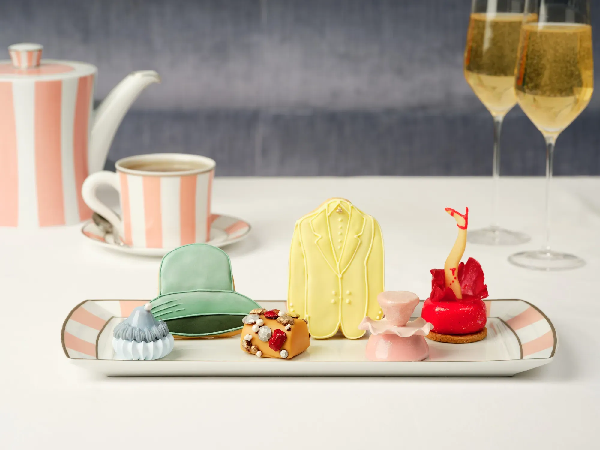 Assorted fashion‑inspired pastries on a tray with striped teaware and two glasses of champagne.