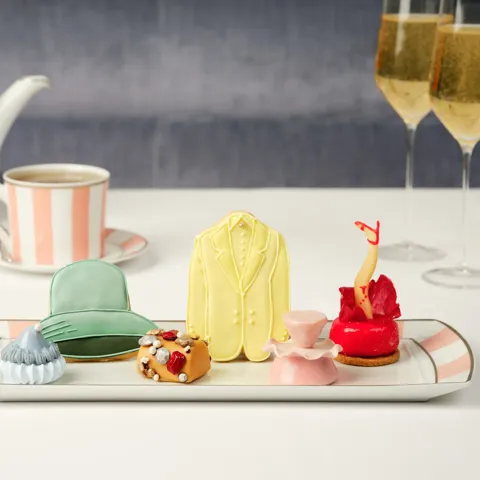 Assorted fashion‑inspired pastries on a tray with striped teaware and two glasses of champagne.
