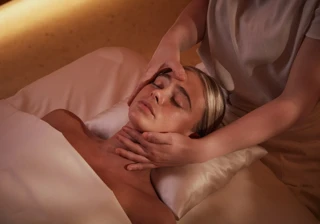 Guest receiving facial massage at spa, lying on pillow under soft warm lighting.