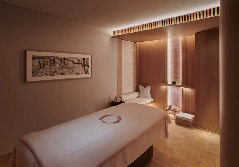 A clean treatment room with a padded table, soft lighting, and neatly arranged medical or wellness equipment.