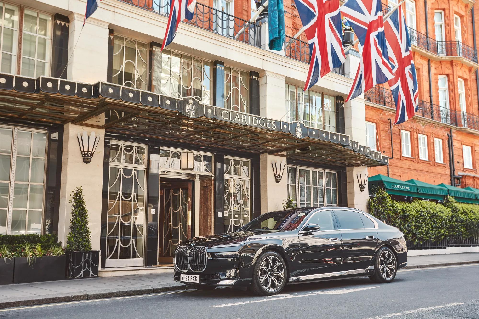 A sleek black BMW parked outside the Art Deco entrance of Claridge’s hotel in London, with Union Jack flags hanging above and the red-brick building visible in the background.