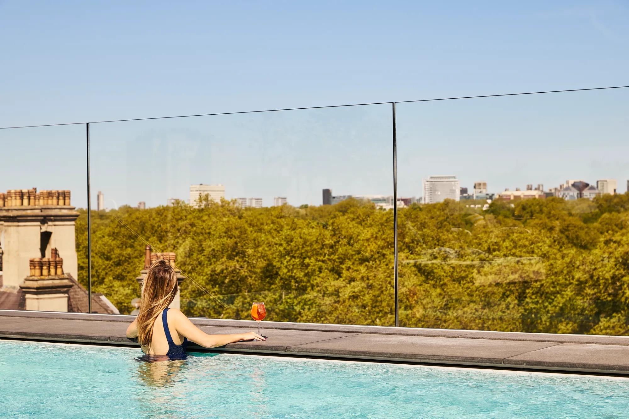 A woman standing in the pool with a cocktail looking at the view