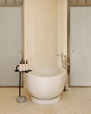Salle de bain moderne avec baignoire ovale autoportante, robinetterie chromée élégante et petite table avec produits de toilette de luxe.
