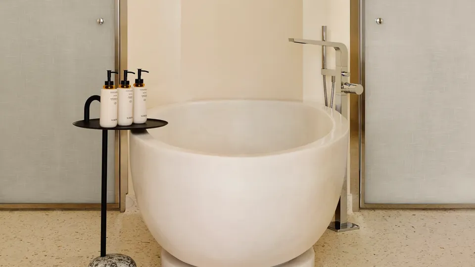 Modern bathroom with a freestanding oval bathtub, sleek chrome fixtures, and a side table holding luxury toiletries.
