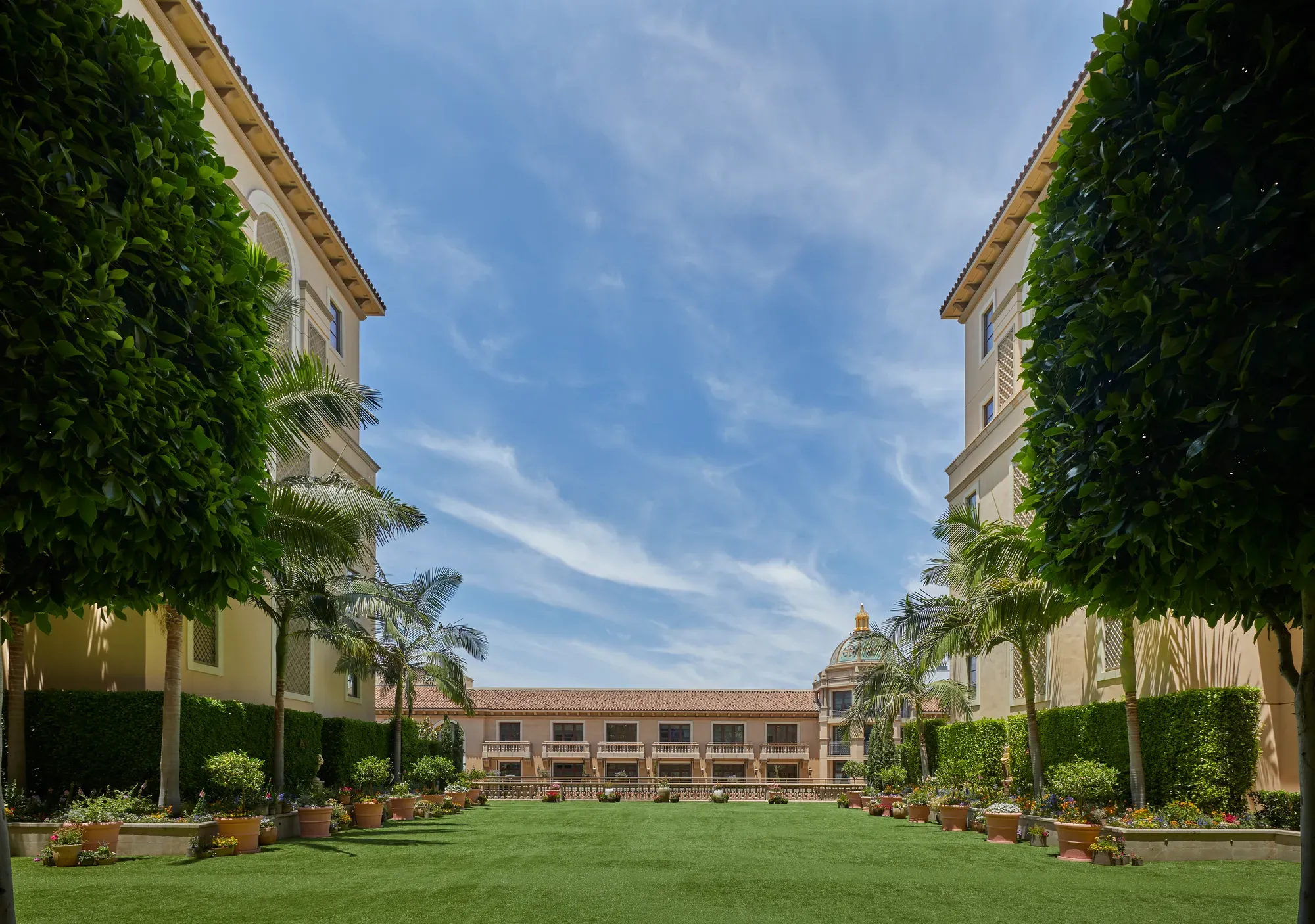 Garden Terrace lawn framed by palms and potted flowers, with domed rooftop of Beverly Hills beyond under a bright blue sky.