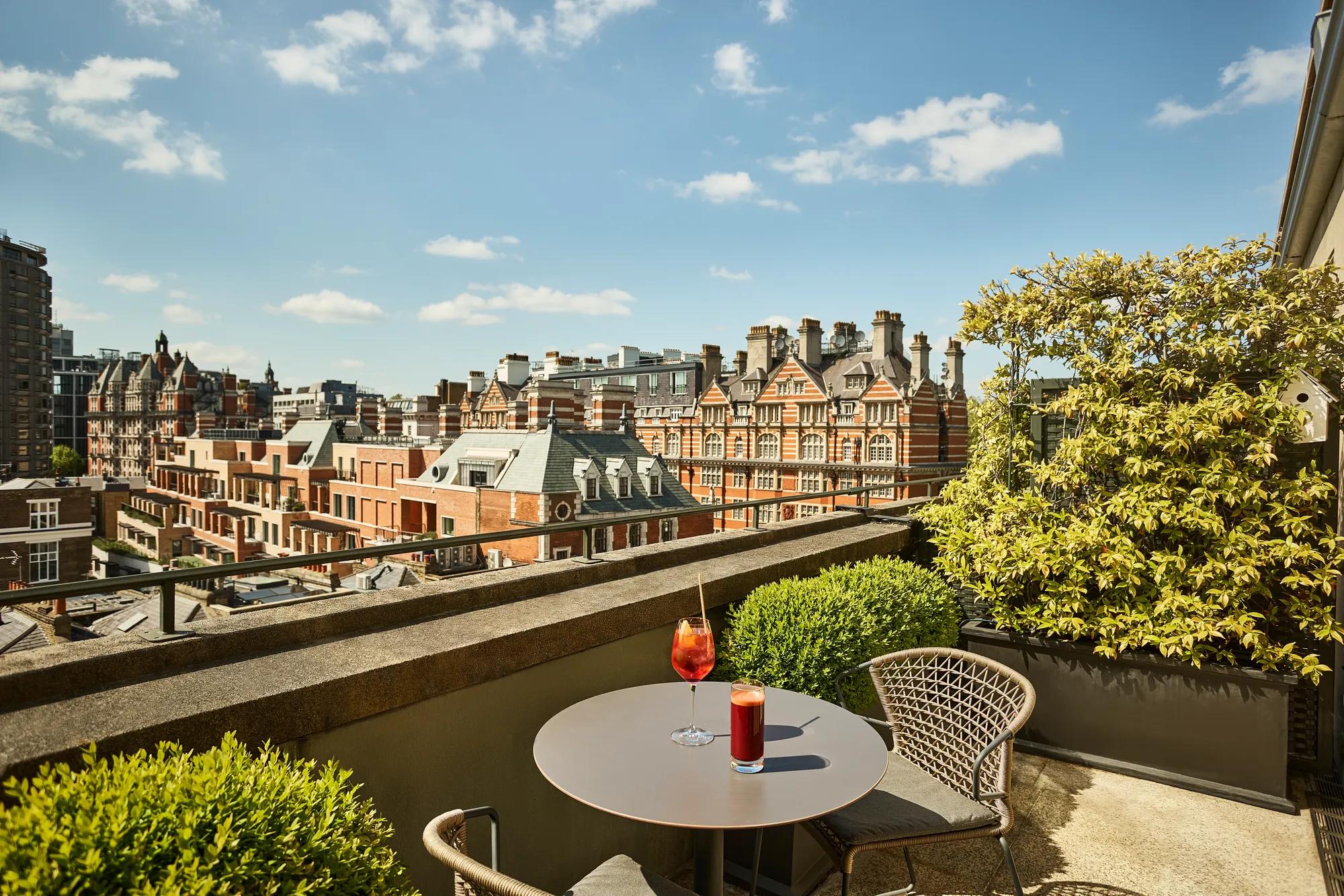 Terrace seating area with drinks overlooking historic rooftops and red-brick buildings beneath a blue sky.