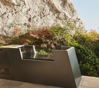 Modern outdoor ice bath beside landscaped greenery and a stone cliff wall.