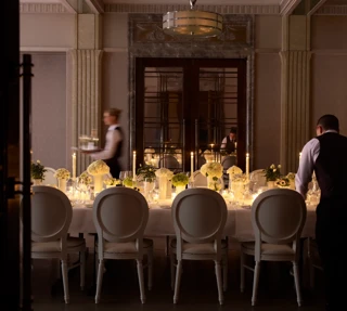 Elegant private dining room with a long candlelit table, floral centrepieces, and staff preparing place settings.